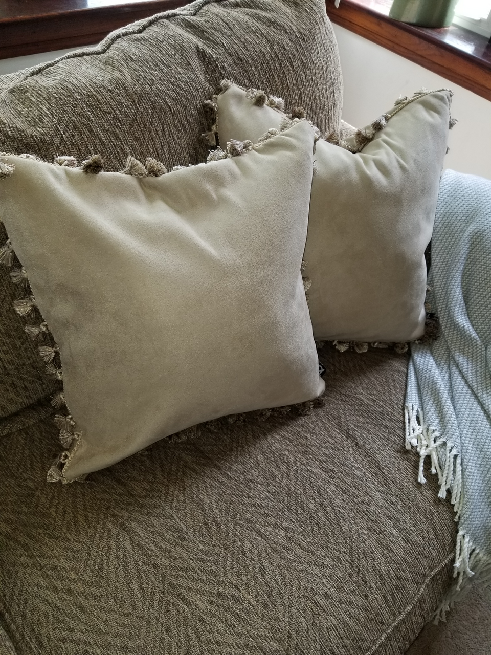taupe velour fabric pillow covers with matching pom pom fringe trim on tan couch with taupe throw cover