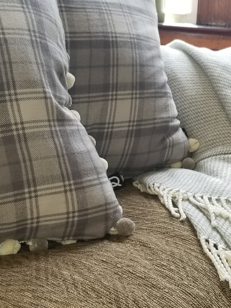 gray plaid pom pom pillow covers on tan couch with taupe throw cover close up
