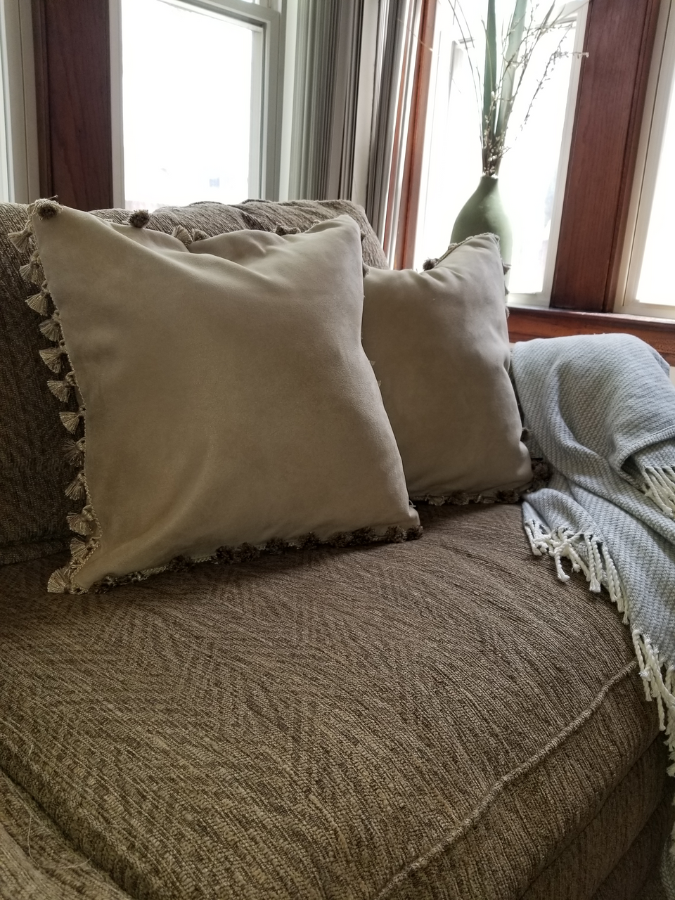 taupe velour fabric pillow covers with matching pom pom fringe trim on tan couch with taupe throw cover