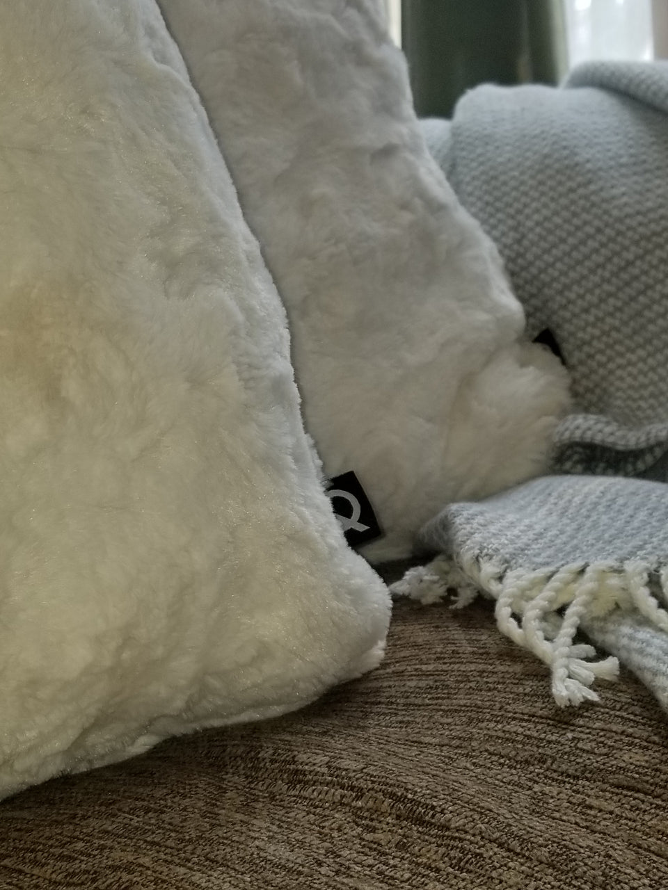 soft faux fur throw pillow cover on tan couch with taupe throw cover closeup