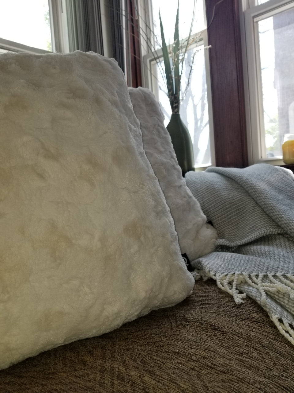 soft faux fur throw pillow cover on tan couch with taupe throw cover closeup