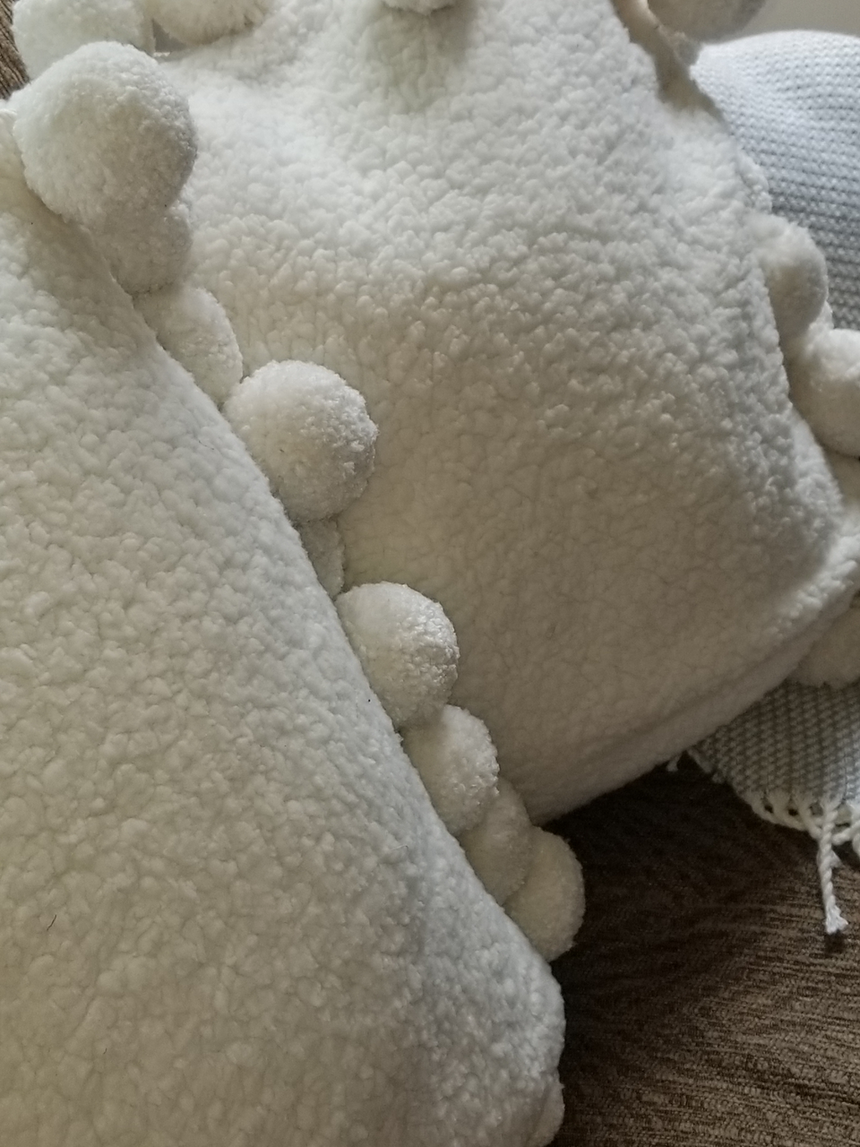 cream sherpa fleece jumbo pom pom pillow covers on a tan couch with taupe throw cover