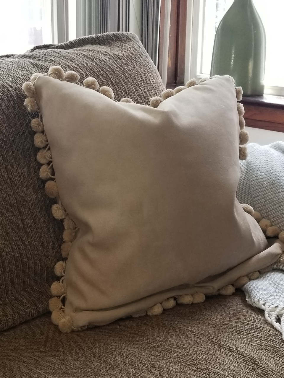 taupe velour fabric pillow covers with matching fur pom pom fringe trim on tan couch with taupe throw cover