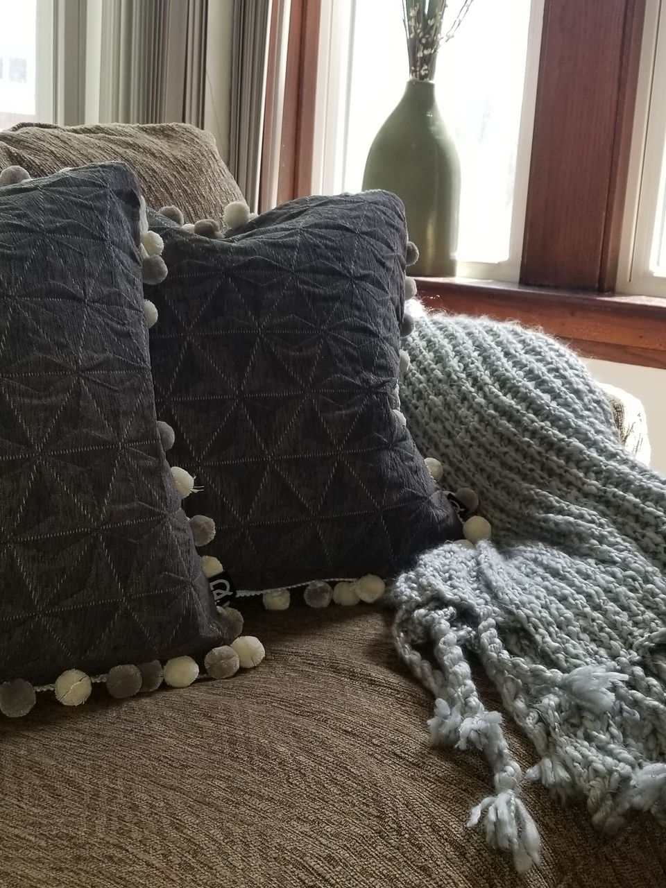 gray textured pillow covers with pom pom trim on taupe couch with knitted gray throw cover closeup