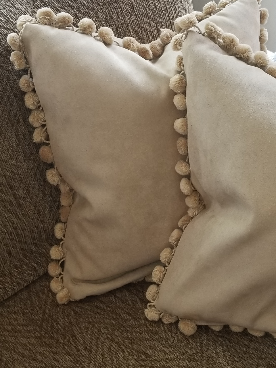 taupe velour fabric pillow covers with matching fur pom pom fringe trim on tan couch with taupe throw cover closeup