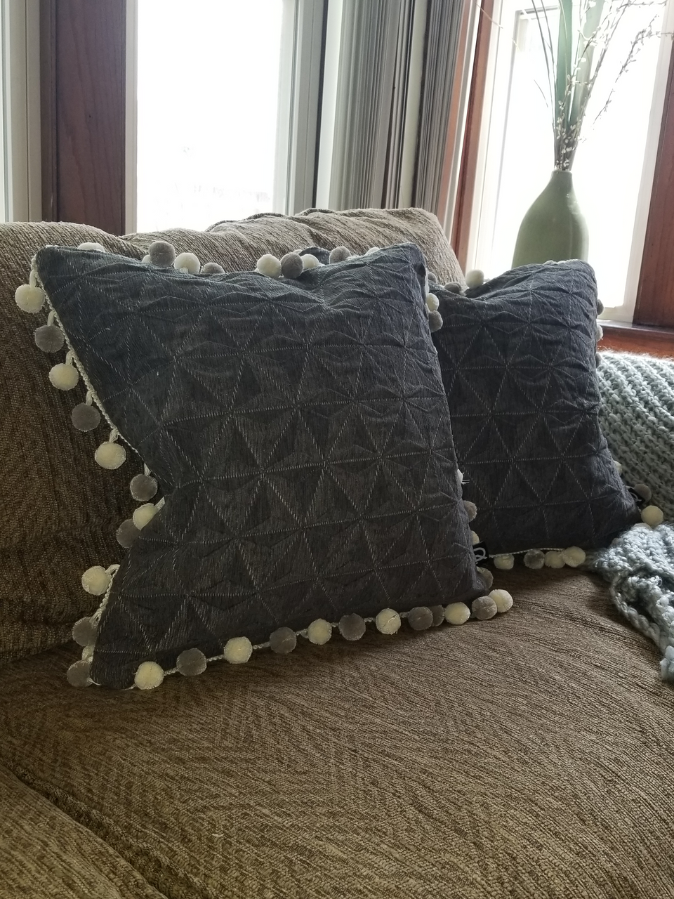 gray textured pillow covers with pom pom trim on taupe couch with knitted gray throw cover