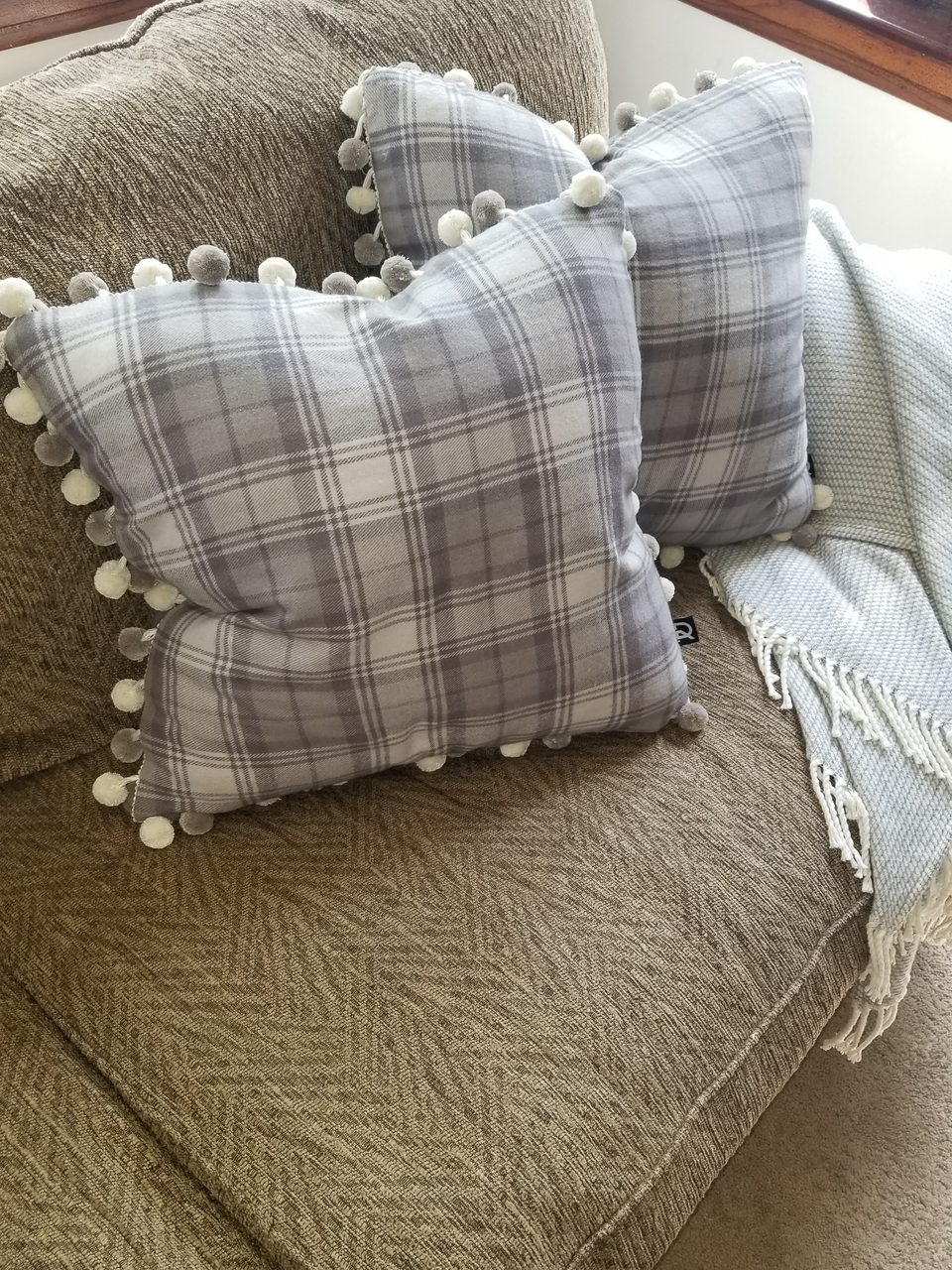 gray plaid pom pom pillow covers on tan couch with taupe throw cover