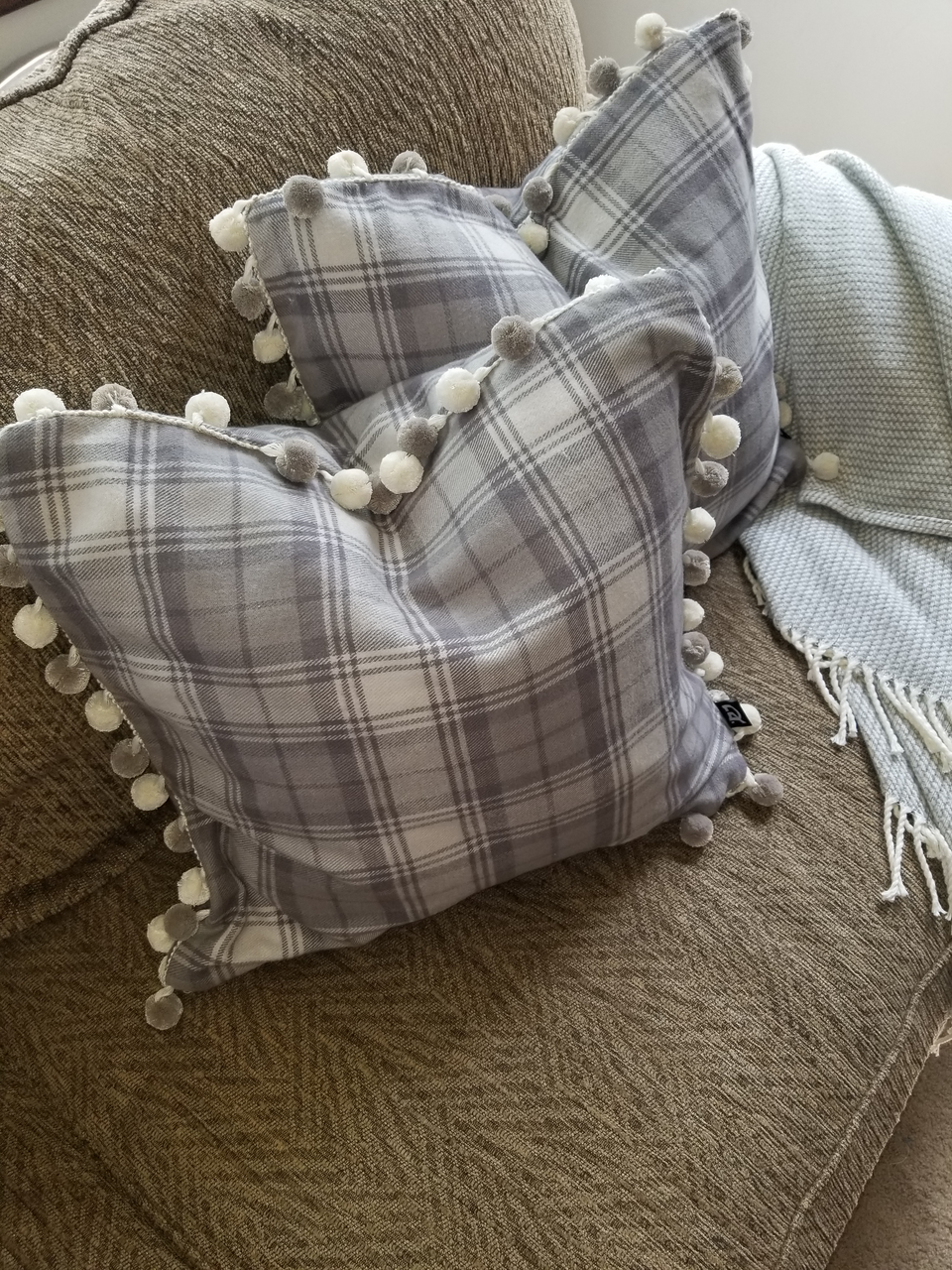 gray plaid pom pom pillow covers on tan couch with taupe throw cover top view