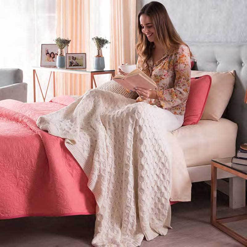 cable knitted beige throw blanket in use by woman on bed
