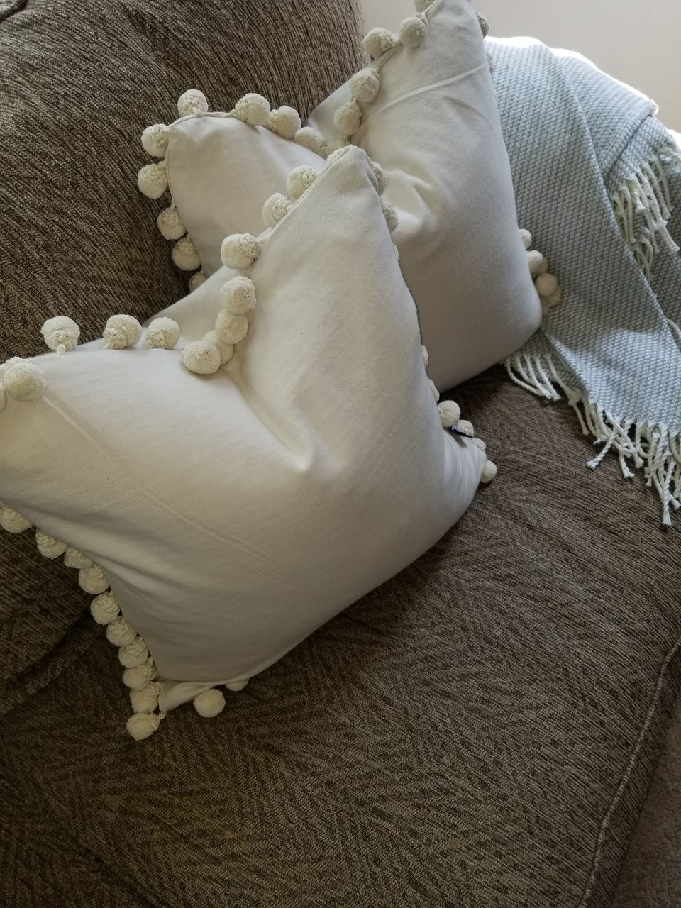 18 x 18 cream pom pom pillow covers on brown couch with beige throw cover top view