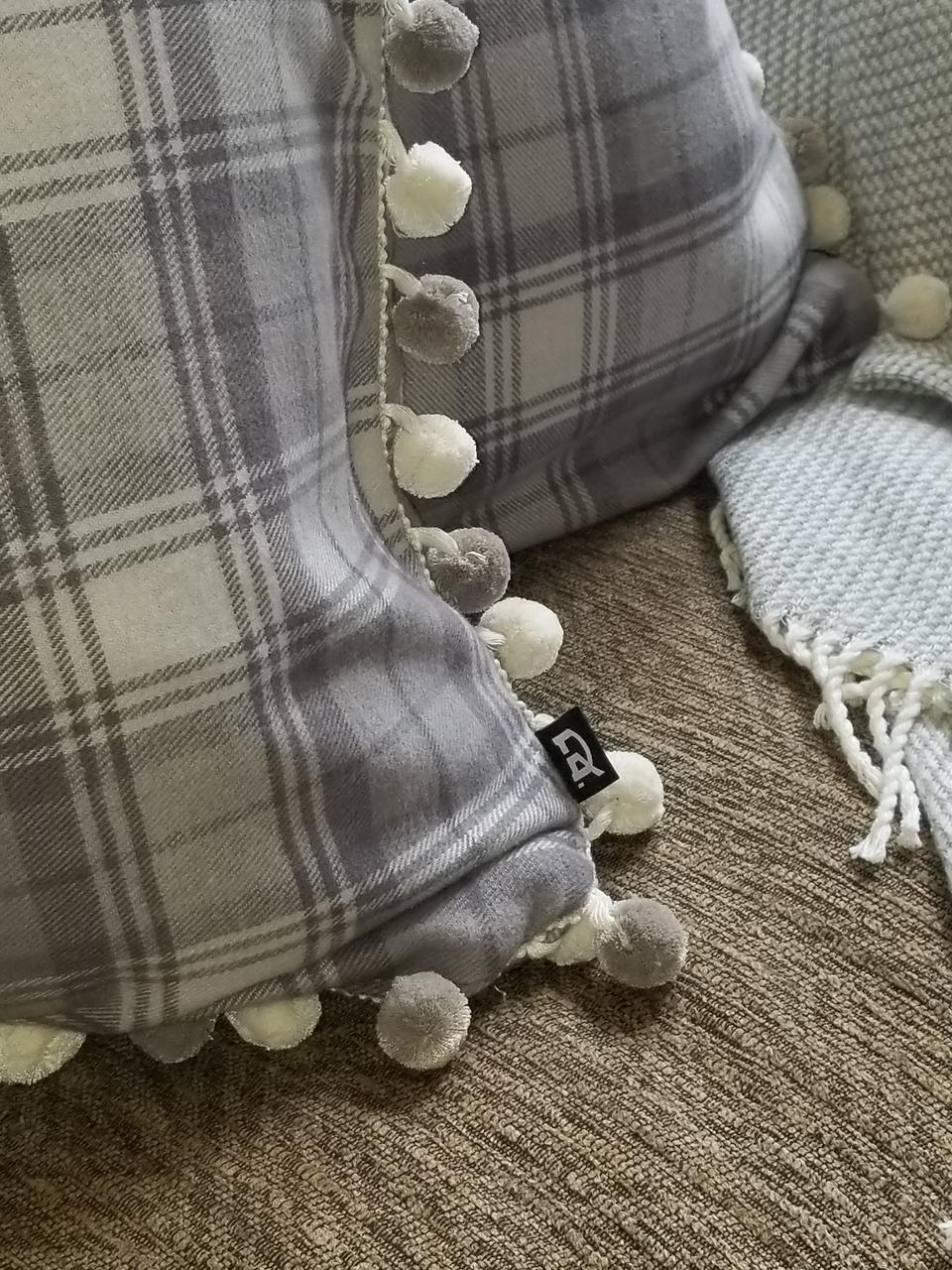 gray plaid pom pom pillow covers on tan couch with taupe throw cover