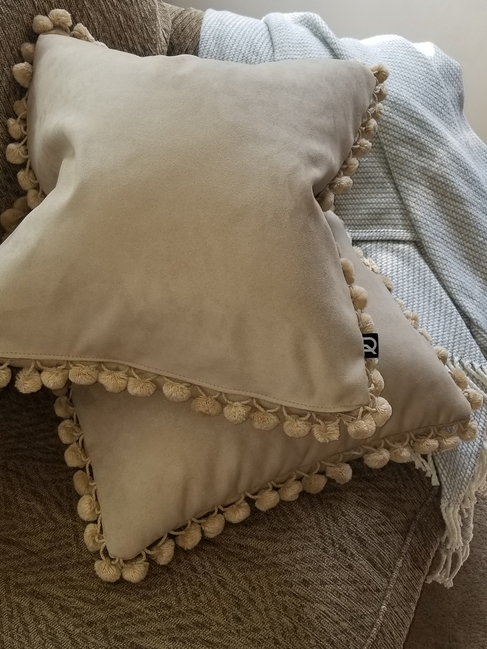 taupe velour fabric pillow covers with matching fur pom pom fringe trim on tan couch stacked