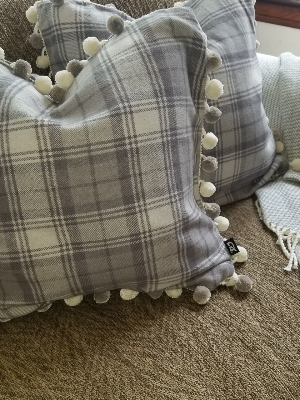 gray plaid pom pom pillow covers on tan couch with taupe throw cover