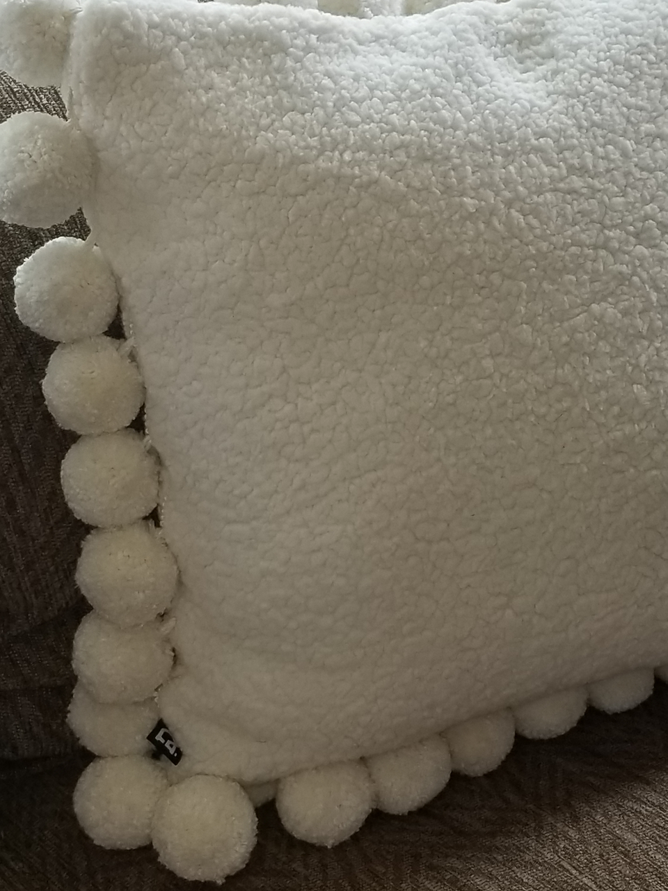 cream sherpa fleece jumbo pom pom pillow covers on a tan couch closeup
