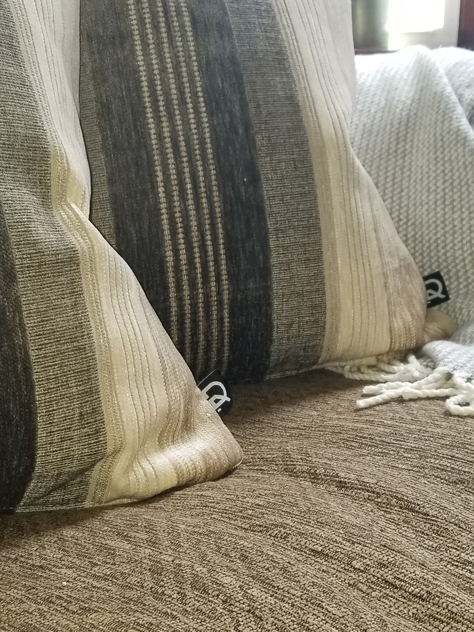 taupe and ivory velour stripe pillow covers on brown couch with taupe throw cover closeup