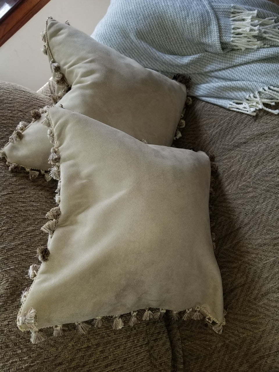 taupe velour fabric pillow covers with matching tassle trim on tan couch with taupe throw cover